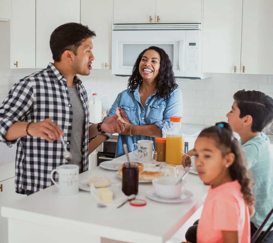 A family of four laugh while eating breakfast around an island