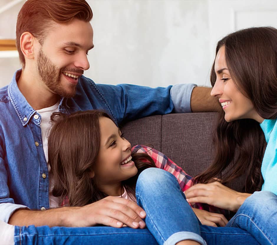 A father, mother, and daughter happily snuggle together on a couch