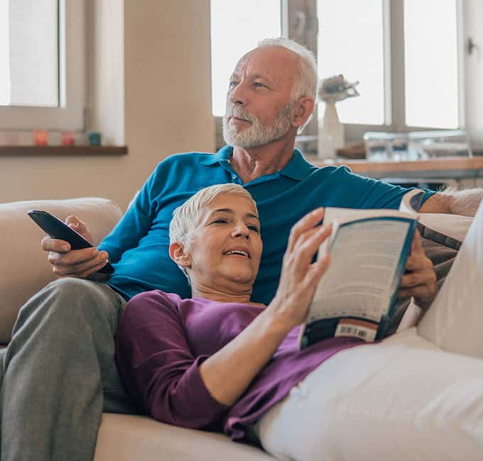 Couple together on the couch, man watching tv, woman reading