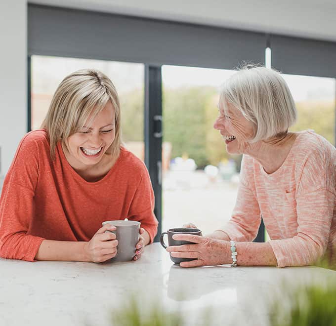 Adult daughter and mother laughing over coffee