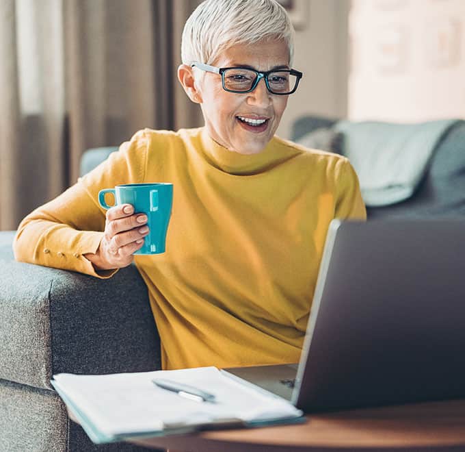 Older woman holding mug and smiling while looking at a laptop